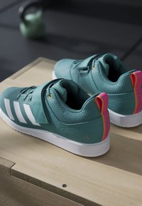 Tyrkysové športové topánky s bielymi pruhmi, textúrovaný materiál, plochá podrážka a ružové a oranžové akcenty na päte, navrhnuté pre výkon.