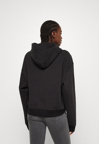 Melnā īsā hoodie ar kapuci, ar regulējamu saiti, ribota apakšmala un garām piedurknēm. Gluda tekstūra, brīva piegriezuma un minimālistisks dizains.