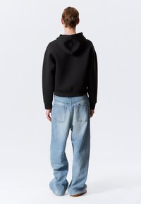 Sort hætte sweatshirt og lyseblå løstsiddende jeans med en falmet tekstur, der har baglommer og en afslappet silhuet.