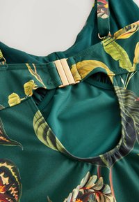 Groene stoffen swimsuit met tropische bladraden, gouden hardware sluiting en open achterkant ontwerp. Effen textuur, verstelbare bandjes.