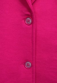Fuchsiový cardigan na knoflíky se značkovou texturou a dvěma kulatými, ladícími knoflíky. Vertikální šev zvýrazňuje přední design.