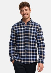Camisa de franela a cuadros en azul marino, azul claro y marrón. Presenta un cuello de botón y botones en la parte delantera, con mangas largas y un corte holgado.