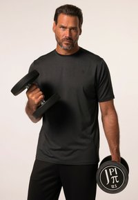 T-shirt atletico nero con collo rotondo e maniche corte, abbinato a pantaloni neri. L'uomo tiene due manubri, uno dei quali è etichettato "12,5".