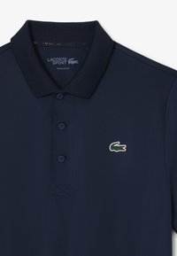 Navyblå polo skjorta i mjukt tyg, med klassisk krage, tre knappar och en liten broderad krokodil-logotyp på bröstet.