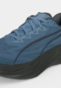 Chaussure de sport bleue avec tige en mesh, design en zigzag près des lacets et semelle noire épaisse, vue de côté extérieur.