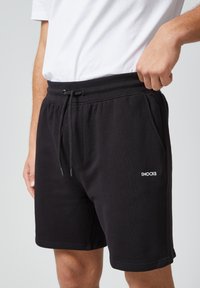 Zwarte katoenen shorts met een elastische tailleband, koordsluiting en zijzakken. Voorzien van een wit "SNOCKS"-logo op het been.
