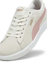 Weiße Wildleder-Sneaker mit einem rosa Streifen, ausgestattet mit einer strukturierten Oberfläche, runder Zehenpartie, flachen Schnürsenkeln und einer weißen Gummisohle. Akzente in Gold.