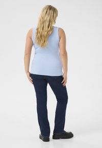 Hellblaues ärmelloses Oberteil mit gerippter Textur, kombiniert mit dunkelblauen geraden Jeans. Schwarze Plateauschuhe, gestylt mit langen, welligen Haaren.