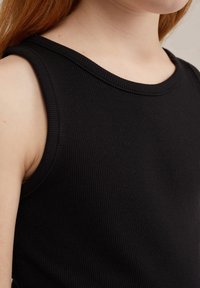 Juodos juostelės marškinėliai su apvaliu iškirpimu ir plačiomis petnešėlėmis, pasižymintys lygiu paviršiumi ir prigludusia danga. Nėra akcentų ar išskirtinių raštų.