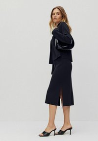Svart stretchkjol med medellång skirt och sidsspringa, i kombination med en svart kort jacka och svarta öppna klackar.