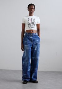 White cropped t-shirt with "Palm Angels" print, paired with light blue jeans featuring a graphic design with "Los Angeles" text. Black shoes.