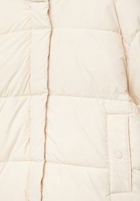 Giacca a vento color crema con texture trapuntata, dotata di tasca con bottone sul lato e cucitura verticale sul davanti.