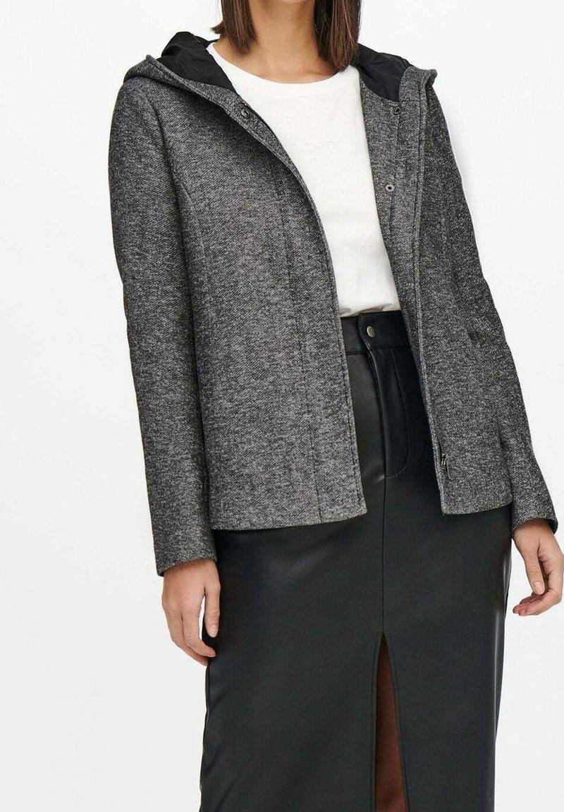 Grå tekstureret jakke med sort hætte, lynlås foran og to sidelommer, kombineret med en hvid skjorte og et sort lædernederdel med en slids.