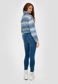 Blau gestrickter Rollkragenpullover mit gestuften Streifen, kombiniert mit figurbetonten blauen Jeans und weißen Sneakern mit strukturierten Sohlen.