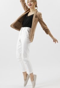 Beige blazer over een zwart kanten tanktop, gecombineerd met witte high-waisted broeken en beige instapschoenen met uitsnijdingen.