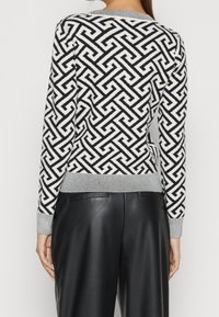 Zwart-wit gebreide trui met een geometrisch patroon, geribbelde grijze manchetten en een ronde halslijn. Draagt zwart leren broek.