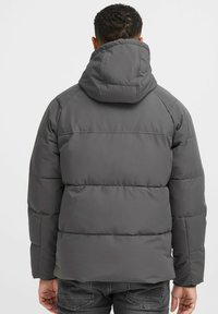 Jachetă puffer gri închis cu glugă, având segmente orizontale quiltate și o textură de țesătură netedă. Fără logo-uri sau modele vizibile.