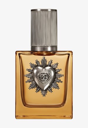 Flacon de parfum rectangulaire ambre avec un emblème en forme de cœur argenté et un motif de rayons de soleil, surmonté d'un grand bouchon argenté cannelé.