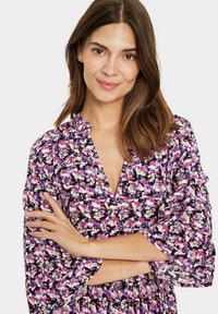 Rochie florală cu un fundal negru, cu modele în nuanțe de mov, roz și verde, decolteu în formă de V și mâneci clopot trei sferturi.