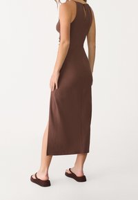 Brun, tætsiddende midi kjole med rund halsudskæring, nøglehul bagdetalje og sidesplit. Lavet af blødt, struktureret stof. Sammen med mørkebrune sandaler.