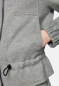 Graue, strukturierte Fleecejacke mit Reißverschluss vorne, elastischen Bündchen und Seitentaschen. Verfügt über einen Kordelzug am Saum zur Anpassung.