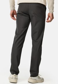Pantalons de sport légers de couleur gris foncé avec une texture lisse et une coupe ajustée, assortis de baskets blanches et grises.
