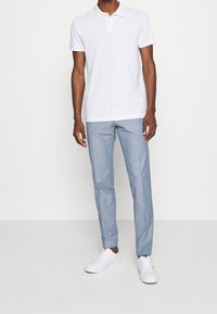 Polo shirt blanc avec col, associé à un pantalon bleu clair et des baskets blanches. Le polo est doté une patte de boutonnage à deux boutons.