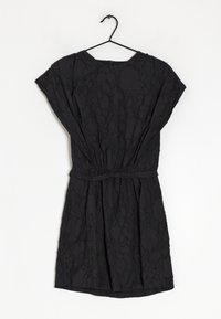 Robe noire en matériau texturé, avec des manches courtes, une taille élastique et une coupe ample, suspendue à un crochet noir.