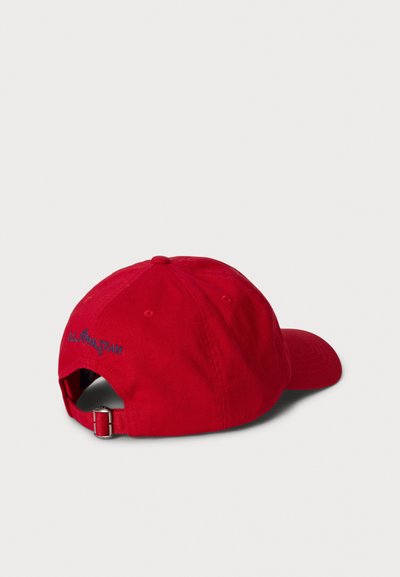 Rdeča baseball kapa z nastavljivo kovinsko zaponko in modrim vezenim napisom "RL POLO TEAM" na zadnji strani, na enobarvnem svetlem ozadju.