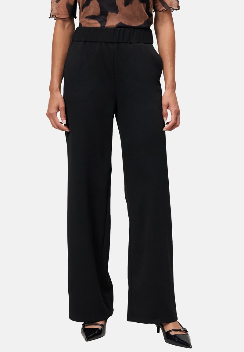 Pantalons noirs à jambes larges avec une taille élastique, fabriqués à partir d'un matériau doux. Présentent une texture lisse et des lignes épurées.