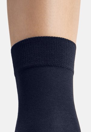 Marinblå ankelsocka med en texturerad, ribbad kant. Tillverkad av ett mjukt, vävt material som har en snug passform. Inga mönster eller ytterligare accenter synliga.
