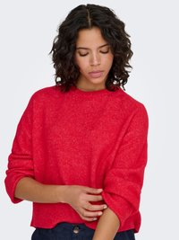 Pull en maille rouge avec une coupe décontractée, un col rond et des manches retroussées. Texture douce avec un motif moucheté subtil.