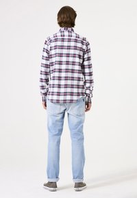 Gevlekt overhemd in wit, rood en marineblauw; lichtgewicht stof. Gecombineerd met lichtblauwe jeans en grijze schoenen, bekeken vanaf de achterkant.