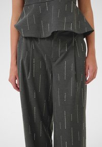 Sivi peplum top s točkomastim uzorkom i odgovarajućim širokim hlačama. Tkanina je glatka; točkice su metalne i ravnomjerno raspoređene po površini.