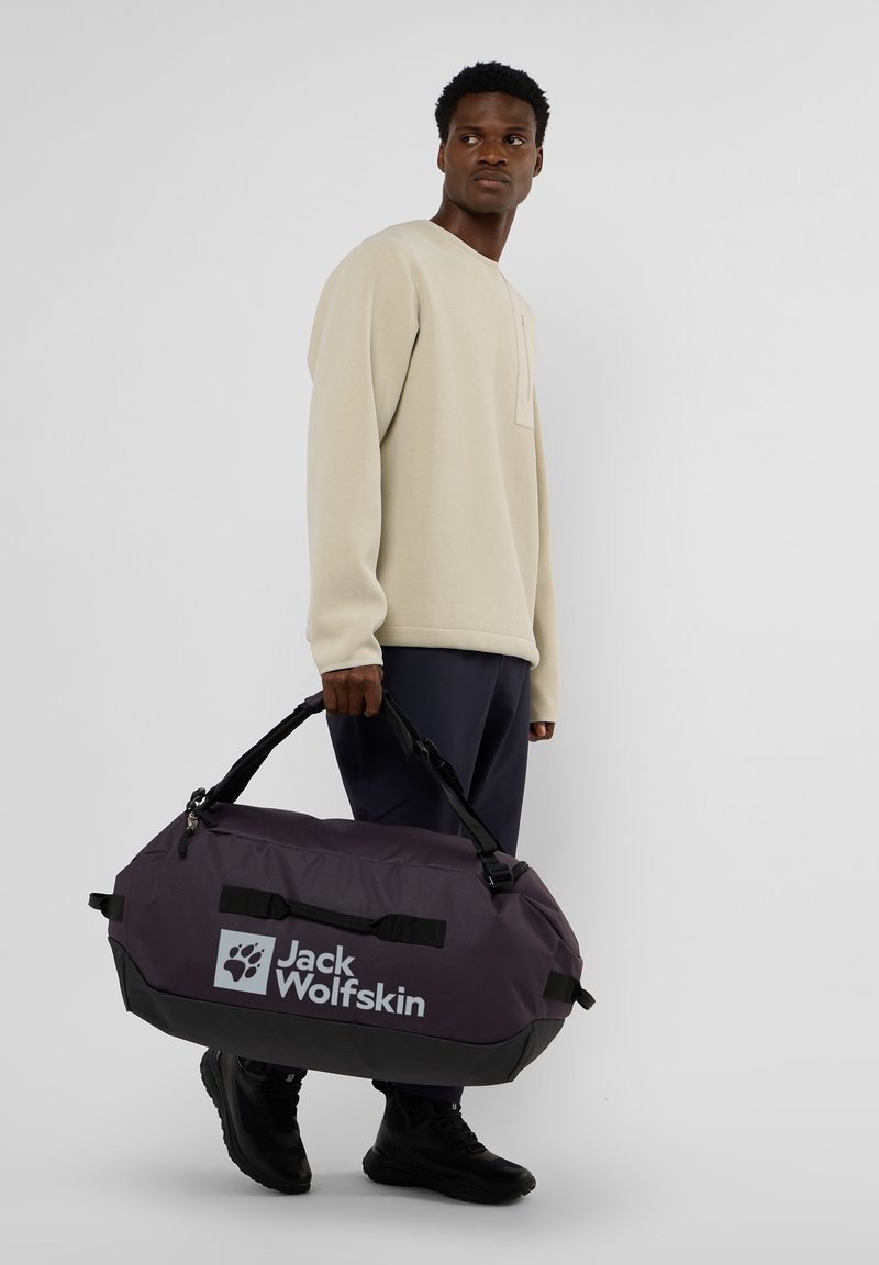 Borsa a viaggio viola con base nera, caratterizzata da logo e manici neri. Il materiale sembra resistente e impermeabile, adatto per i viaggi.
