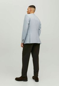 Giacca di suit blu chiaro con vestibilità slim, uno spacco posteriore e pantaloni formali marroni. Dettagli notevoli includono bottoni sui polsini e una texture liscia.