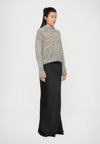 Strikket sweater i blandede grånuancer med høj hals og lange, brede ærmer, parret med en tætsiddende sort satin-nederdel, der falder til gulvet.
