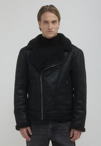 Giubbotto in ecopelle nera con colletto e polsini in shearling. Dotato di chiusura con zip e tasche laterali, offre una finitura testurizzata.