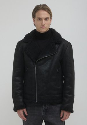 Giubbotto in ecopelle nera con colletto e polsini in shearling. Dotato di chiusura con zip e tasche laterali, offre una finitura testurizzata.