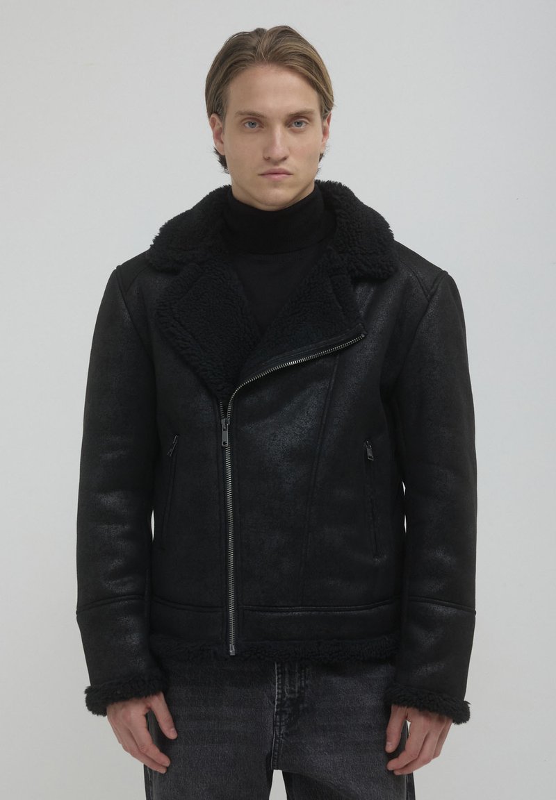 Giubbotto in ecopelle nera con colletto e polsini in shearling. Dotato di chiusura con zip e tasche laterali, offre una finitura testurizzata.