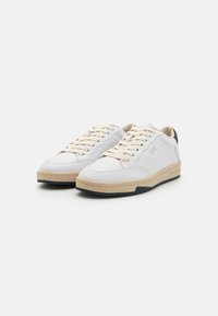 Baskets en cuir blanc avec semelle beige, lacets crème et accent de talon bleu marine. Présente des panneaux latéraux texturés et un logo embossé.