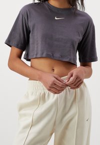 Zkrácené šedé tričko s krátkými rukávy, na hrudi s malým bílým logem Nike, v kombinaci se smetanovými tepláky.