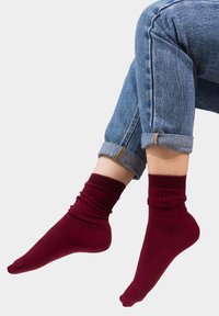 Burgundowe, prążkowane skarpetki do kostek z podwiniętym ściągaczem, wykonane z miękkiego materiału, zaprezentowane na nodze w podwiniętych dżinsach.