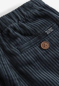Mørkegrå velourstof med lodret ribbing, der har en elastisk talje og en brun knapdetalje med branding på mærket.