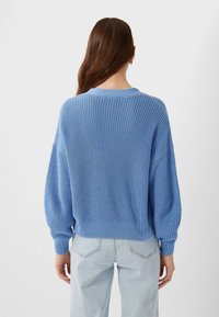 Light blue knitted sweater with loose fit, ribbed texture, and dropped shoulders. Paired with light denim jeans, showing back view.