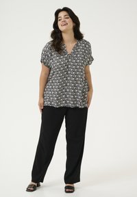 Blouse à motifs noir et blanc avec des manches courtes et un col en V, associée à un pantalon large noir et des sandales à glissière noires.