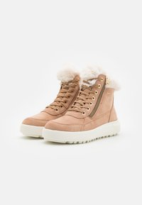 Botas de tobillo de ante color arena con un collar de piel sintética, acentos dorados y cremallera lateral, que cuentan con una suela de goma blanca y un dibujo texturizado.