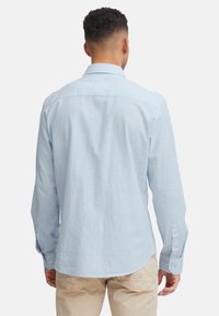 Hellblaues Langarmhemd aus Baumwolle, lässige Passform, mit Knopfmanschetten, Rückenfalten, abgerundeter Saum, glatte Textur.