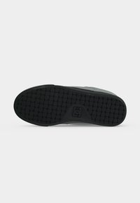 Semelle de chaussure en caoutchouc noir avec un motif diamant texturé et un petit logo géométrique près du centre du talon.