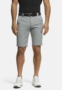 Un short de golf gris avec une texture lisse, des passants de ceinture et une poche avant. Associé à des baskets blanches et un t-shirt noir ajusté.